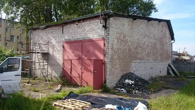 Mały murowany budynek gospodarczy z czerwonymi drzwiami przeznaczony do rozbiórki