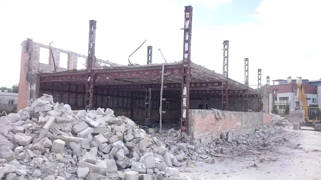 Stalowy szkielet hali ze stertami gruzu i koparką pracującą w tle