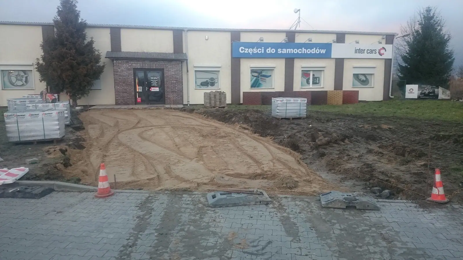 Wyrównana podsypka piaskowa pod chodnik przygotowana do układania kostki brukowej, obok paleta z kostką