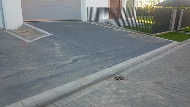 Podjazd z kostki brukowej ze studzienką odpływową i krawężnikiem przy domu jednorodzinnym
