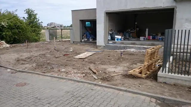 Przygotowany piaszczysty plac pod podjazd z kostką brukową przed otwartym garażem domu
