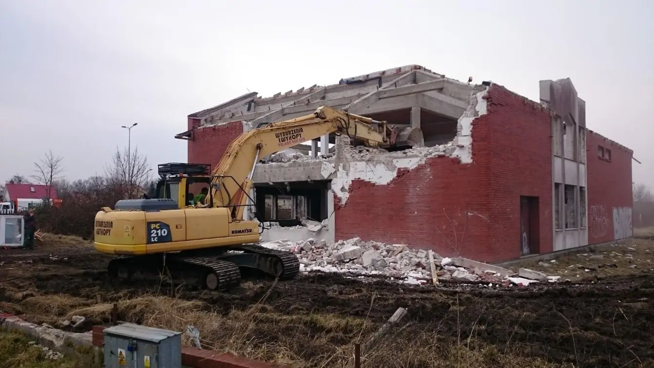 Koparka gąsienicowa Komatsu rozbiera ceglane ściany domu jednorodzinnego w Kołobrzegu podczas rozbiórki budynku