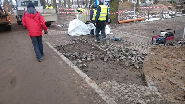 Przechodzień mija ekipę odbudowującą wjazd z kostki brukowej przy skrzyżowaniu w Kołobrzegu