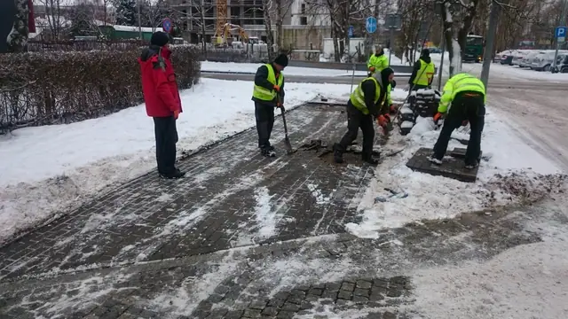 Robotnicy w kamizelkach odblaskowych rozbierają starą nawierzchnię chodnika w śniegu przy ul. Kołłątaja