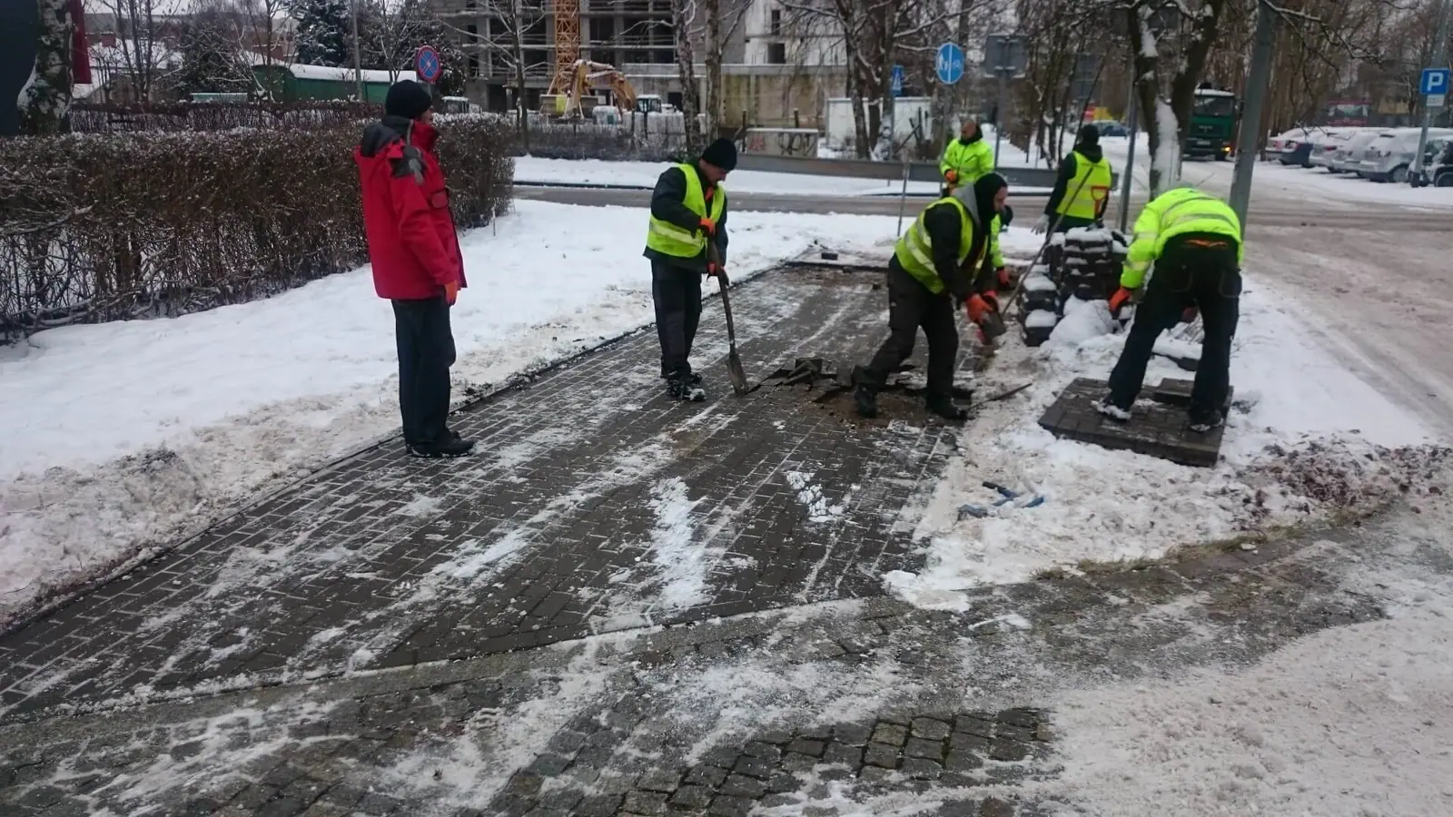 Robotnicy w kamizelkach odblaskowych rozbierają starą nawierzchnię chodnika w śniegu przy ul. Kołłątaja