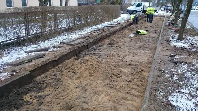 Odsłonięty wykop pod chodnik z odłożonymi płytami betonowymi wzdłuż żywopłotu, resztki śniegu