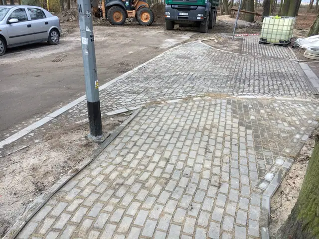 Zakończony fragment chodnika z kostki granitowej wokół latarni, w tle koparka i ciężarówka