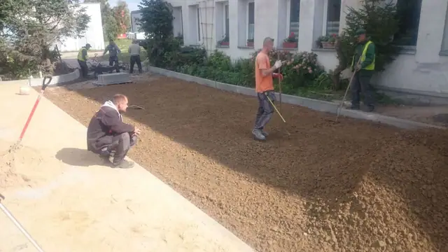 Robotnicy rozprowadzają kruszywo na terenie przed budynkiem wielorodzinnym przy ulicy Sienkiewicza w Kołobrzegu