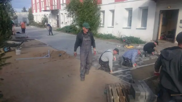 Grupa robotników układa kostkę brukową na chodniku przy budynku na ulicy Sienkiewicza w Kołobrzegu