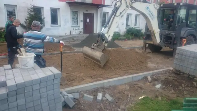 Robotnik uzupełnia spoiny przy krawężniku, obok minikoparka usypuje piasek na ulicy Sienkiewicza w Kołobrzegu