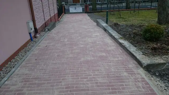 Wybrukowana czerwoną kostką alejka prowadząca do furtki przy ogrodzeniu terenu kościelnego