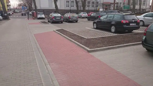 Czerwona kostka brukowa ułożona na wysepce parkingu obok zaparkowanych samochodów