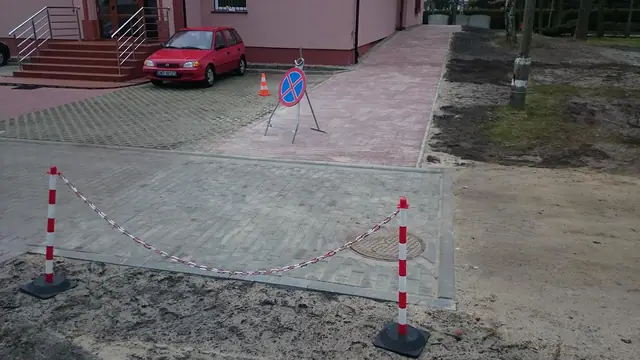 Odgrodzony taśmą fragment wjazdu z czerwonej kostki brukowej z ustawionym znakiem zakazu