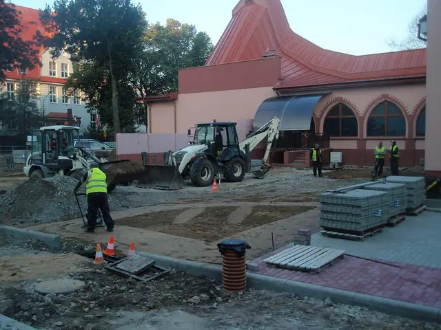 Mini koparka i pracownik przygotowują teren pod kostkę brukową obok różowego budynku kościoła