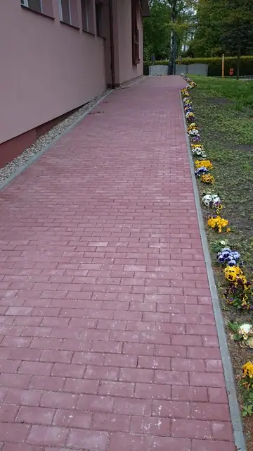Kwitnący rabat kwiatowy wzdłuż czerwonej alejki brukowej prowadzącej do kościoła