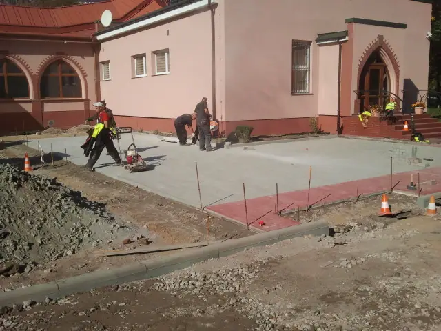 Dwóch robotników zagęszcza świeżą podbudowę betonową przed głównym wejściem do kościoła