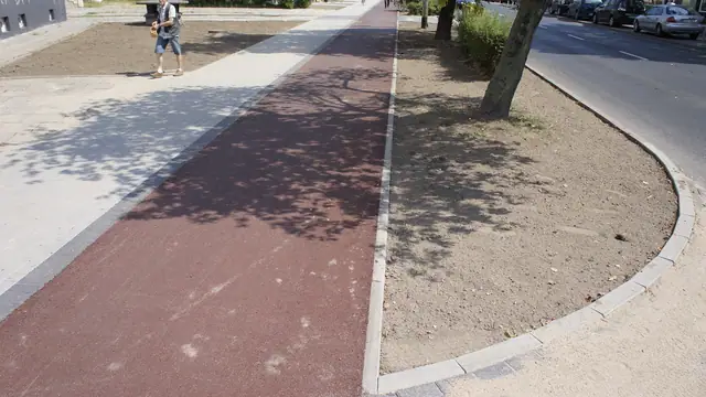 Gotowa czerwona nawierzchnia ścieżki rowerowej wzdłuż zieleńca przy ulicy Zwycięstwa w Koszalinie