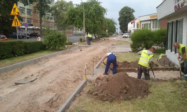 Robotnicy kopią rów pod krawężnik na zieleńcu przy chodniku podczas budowy ścieżki rowerowej w Koszalinie