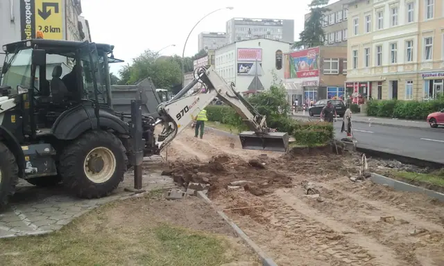 Koparko-ładowarka wykonuje wykop wzdłuż chodnika przy ulicy Zwycięstwa w Koszalinie