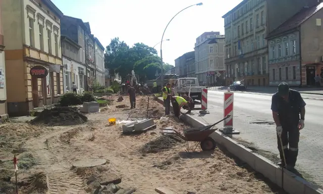 Robotnicy z taczką prowadzą prace ziemne wzdłuż ulicy handlowej podczas budowy ścieżki rowerowej w Koszalinie