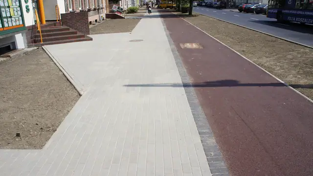 Ścieżka rowerowa i chodnik przed budynkiem z czerwonymi schodami przy ulicy Zwycięstwa w Koszalinie