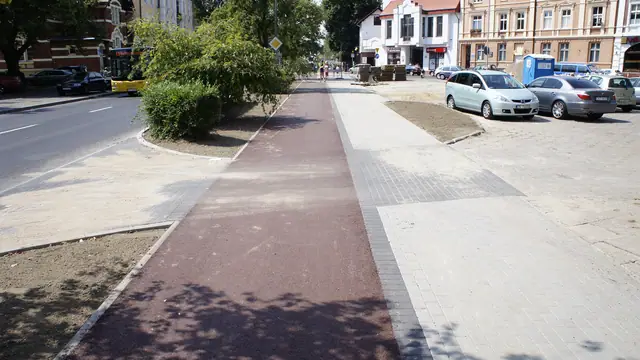 Skrzyżowanie czerwonej ścieżki rowerowej i jasnego chodnika przy parkingu w Koszalinie