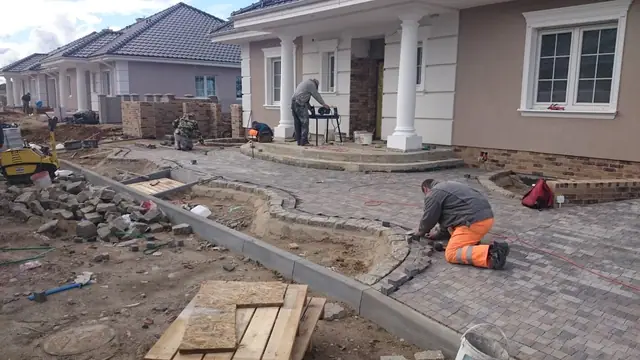 Pracownik układa kostkę brukową na zakrzywionym podjeździe przed ukończoną willą osiedla
