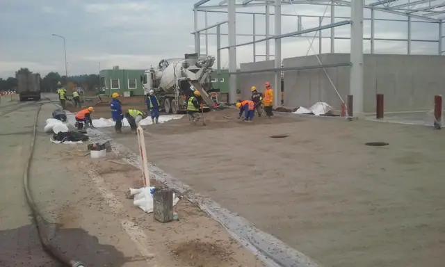 Betonomieszarka wylewa beton przy studzience rewizyjnej, wokół której pracuje ekipa robotników