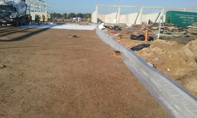 Krawędź wylanej płyty betonowej obramowana czarnym pasem izolacji przy odkrytym gruncie