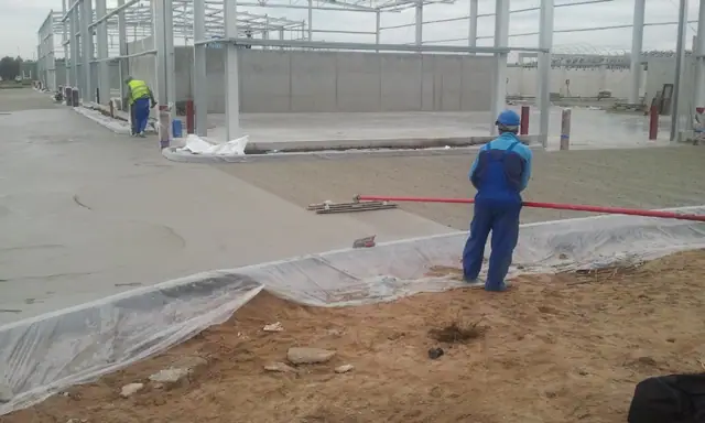 Pracownik ciągnie czerwony wąż po ukończonej jasnoszarej posadzce betonowej wewnątrz hali