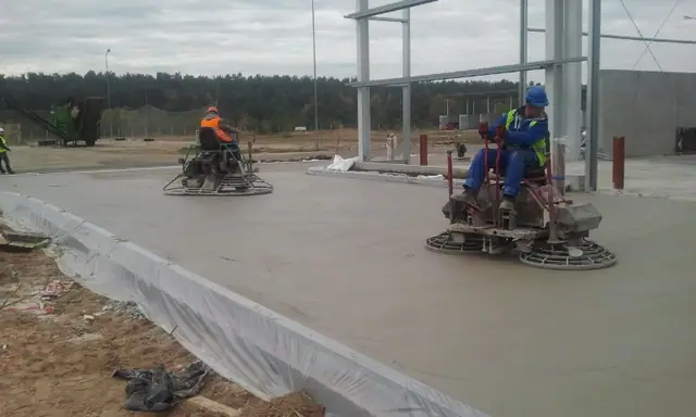 Dwaj operatorzy na zacieraczkach mechanicznych wygładzają świeżą powierzchnię betonową