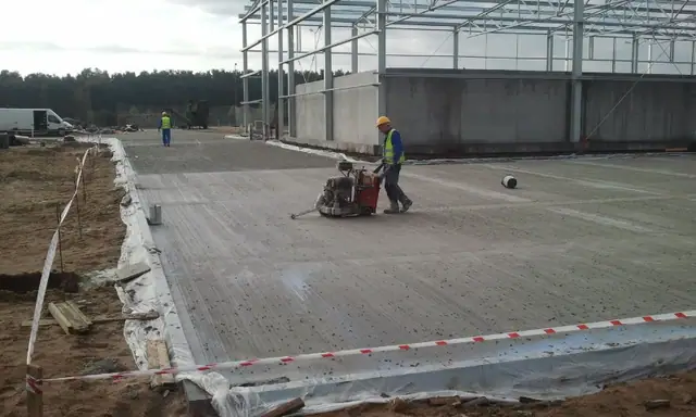 Pracownik zaciera betonową posadzkę zacieraczką wewnątrz stalowej hali w technologii lanego betonu