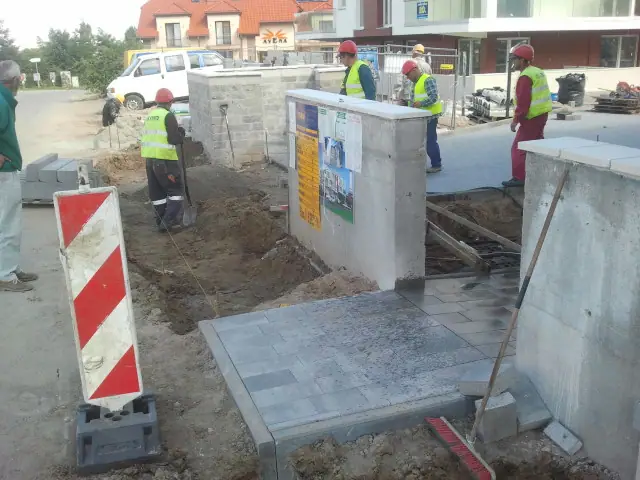 Robotnicy kończą nawierzchnię wokół murowanego słupka osłoniętego barierą ostrzegawczą