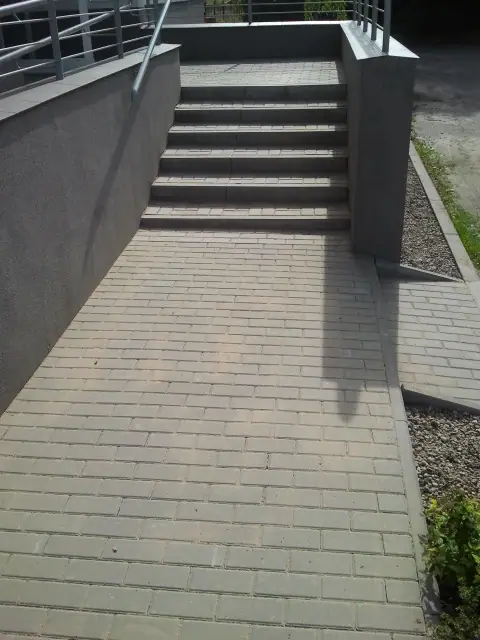 Ukończone schody zewnętrzne z kostki brukowej i szklaną balustradą prowadzące do wejścia