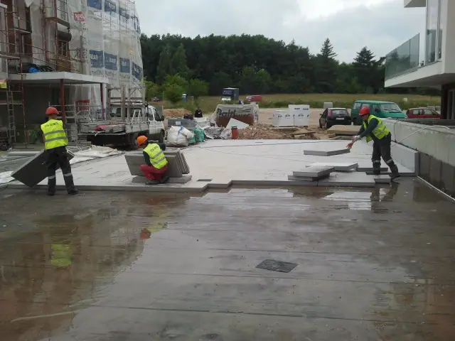 Robotnicy w kamizelkach odblaskowych układają duże płyty betonowe na tarasie przy hotelu Baltic Cliff