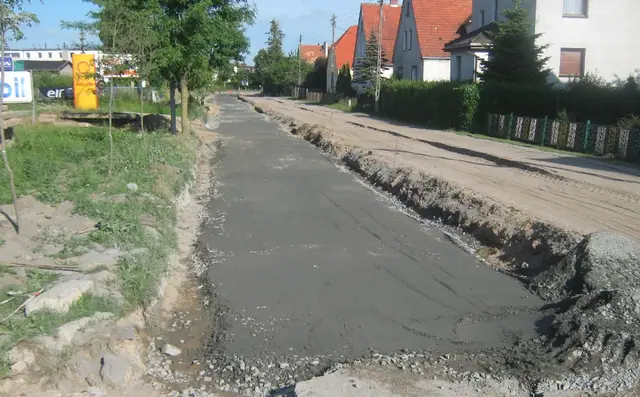 Świeżo ułożona warstwa asfaltu na jednym pasie drogi przy odkrytym poboczu żwirowym