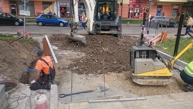 Koparka i zagęszczarka pracują na skwerze w centrum miasta w pobliżu sklepów