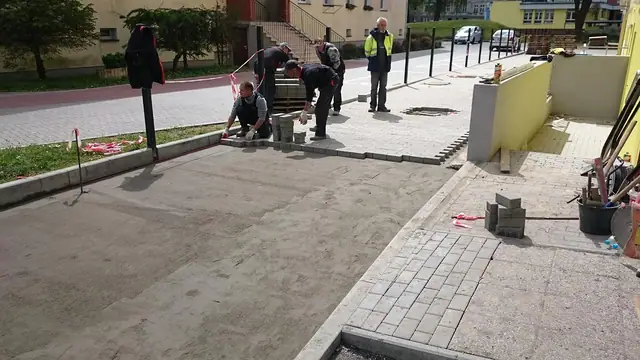 Pracownicy układają kostkę brukową przy nowo osadzonym krawężniku drogi