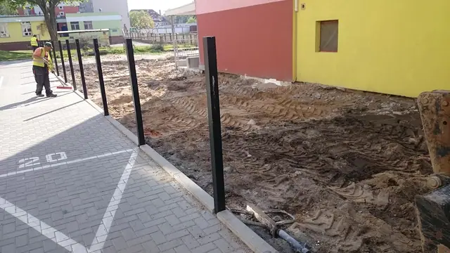 Pracownik wyrównuje grabiami wykop pod nową nawierzchnię obok metalowych słupków
