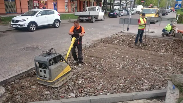 Pracownik zagęszcza nawierzchnię na chodniku w otoczeniu przechodniów