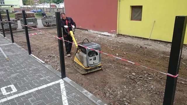 Pracownik z zagęszczarką między nowo osadzonymi słupkami ogrodzeniowymi