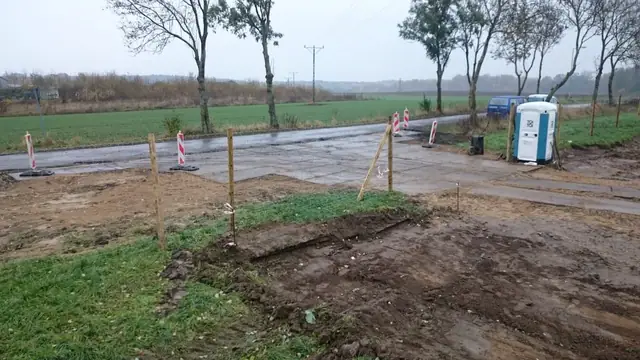 Gruntowa droga dojazdowa do placu budowy z ustawionymi przenośnymi toaletami