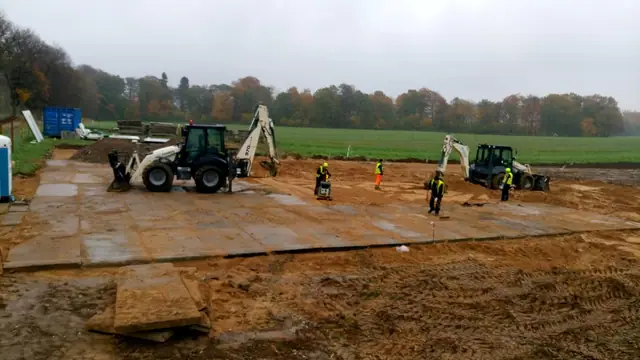 Ekipa układa betonowe płyty drogowe przy użyciu kilku maszyn budowlanych