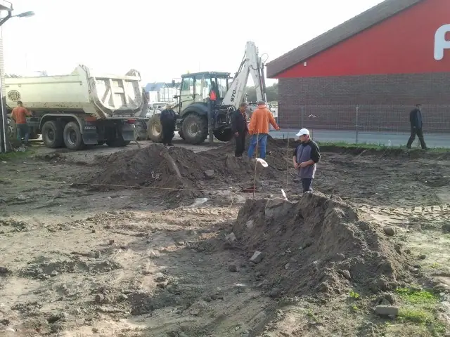 Koparko-ładowarka i robotnicy pracują przy wykopie na zapleczu marketu, obok ciężarówka z gruzem