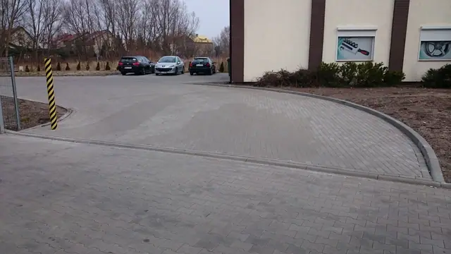 Łukowy wjazd z kostki brukowej na parking przy markecie z zaparkowanymi samochodami