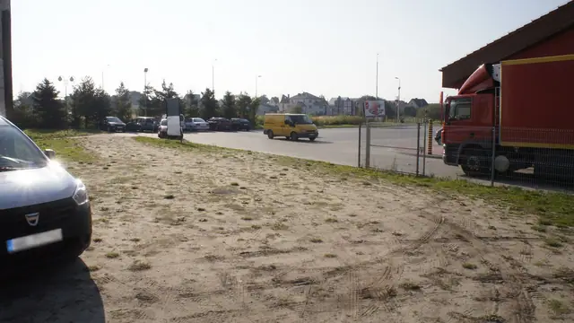 Zarośnięty teren trawiasty obok zaparkowanych samochodów przy budynku marketu