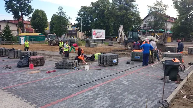 Grupa robotników rozkłada kostkę brukową i studzienki na etapie budowy parkingu