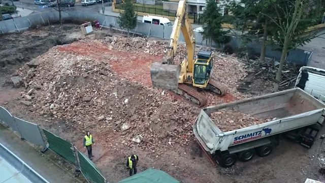 Koparka ładuje gruz na naczepę wywrotki przy stercie ziemi z cegłami