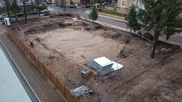 Ogrodzony taśmą pusty plac po rozbiórce budynku, w tle stalowe barierki