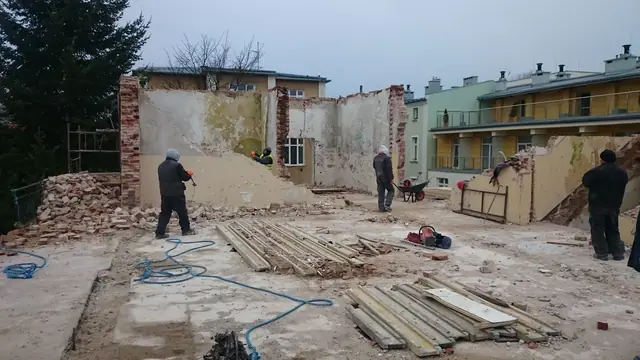 Robotnicy rozbierają murowaną ścianę wewnętrzną wśród stosów gruzu i desek szalunkowych